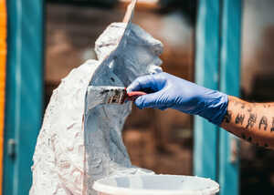 A person with a gloved hand paints a white substance onto a sculpted figure.
